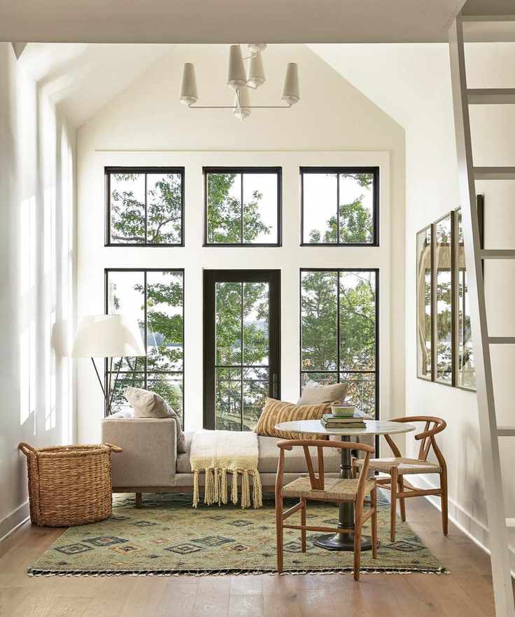 white living space with vaulted ceiling, daybed with throw and cushions, small round dining table and chairs, basket, rug, hardwood floor, floor lamp, view outside