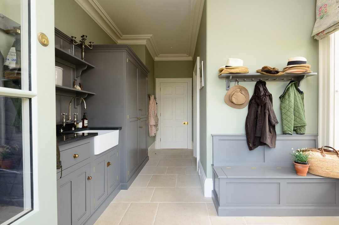 A large mudroom with gray cabinets and a gray wooden bench below coat hooks