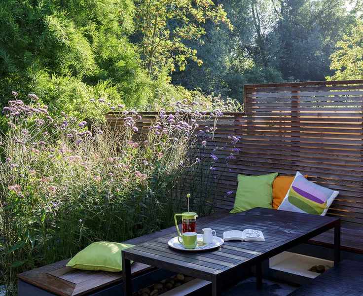 A slatted wooden fence with bushy planting and a black wooden table and bench.