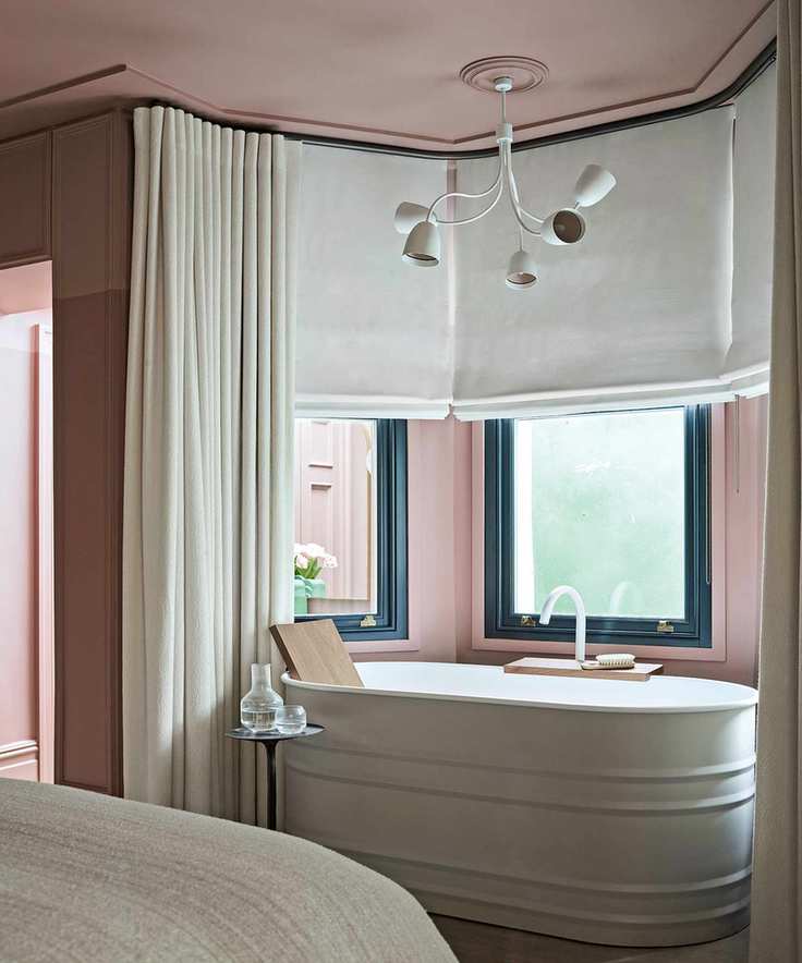 bedroom with pink walls and freestanding curved bath and neutral blinds and curtains