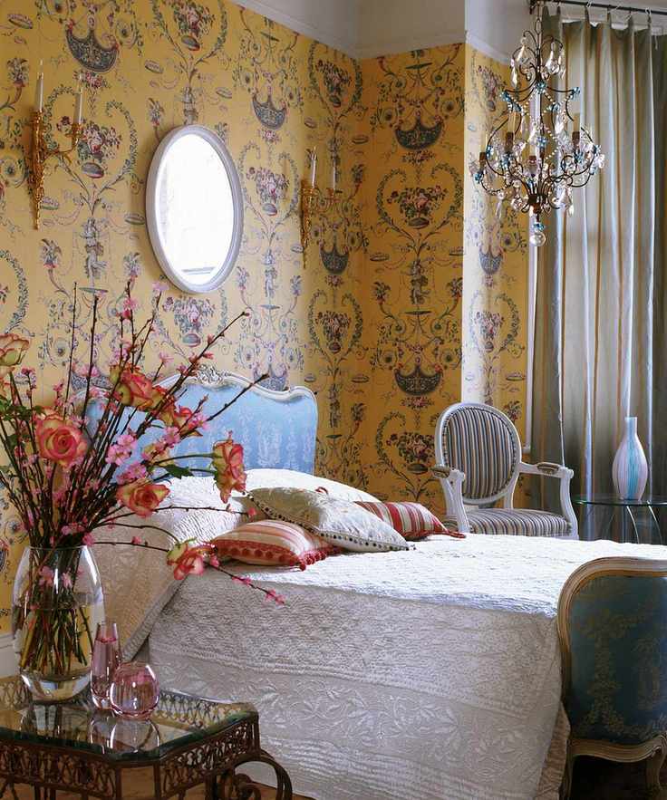 A lively bedroom featuring a chandelier and vibrant rococo-style wallpaper