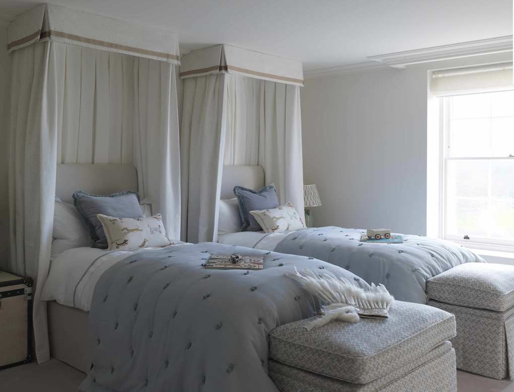 Twin beds with white canopies around headboards and storage space at the ends of the beds showing hotel-style shared bedroom ideas.
