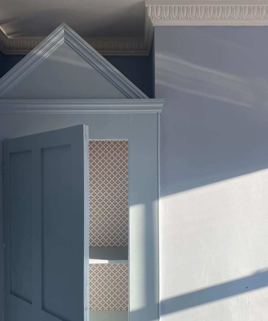 A color-drenched blue room with a cabinet built into the corner, topped with a cabinet hat