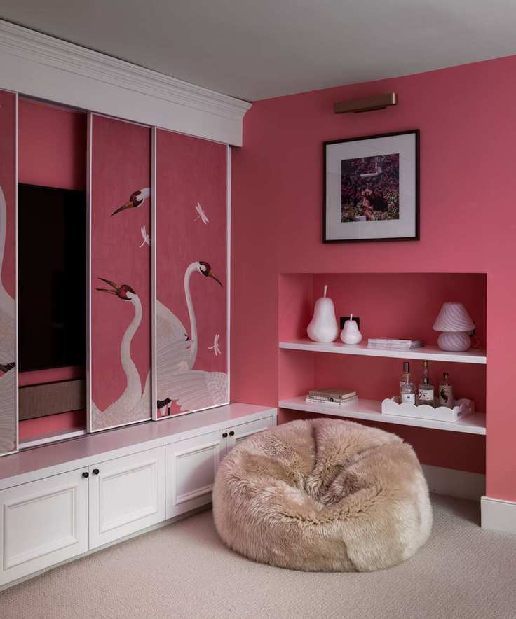 Dark pink painted living room, with bespoke sliding screen with mural, brown beanbag and integrated wall shelving with decorative accessories