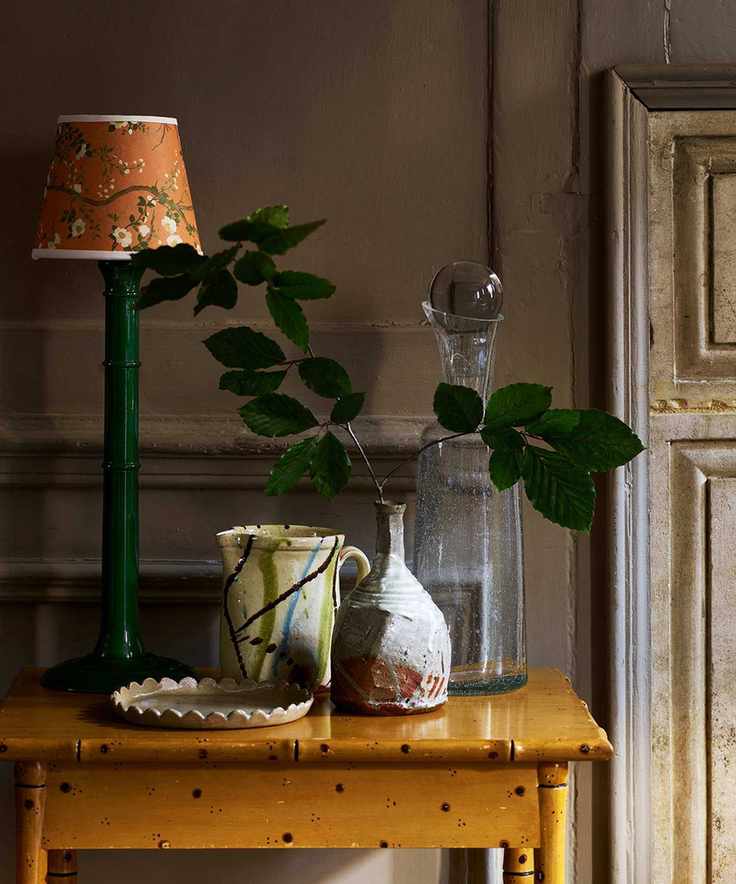 Ochre yellow painted side table with green table lamp, yellow decorative shade and ceramic vessels
