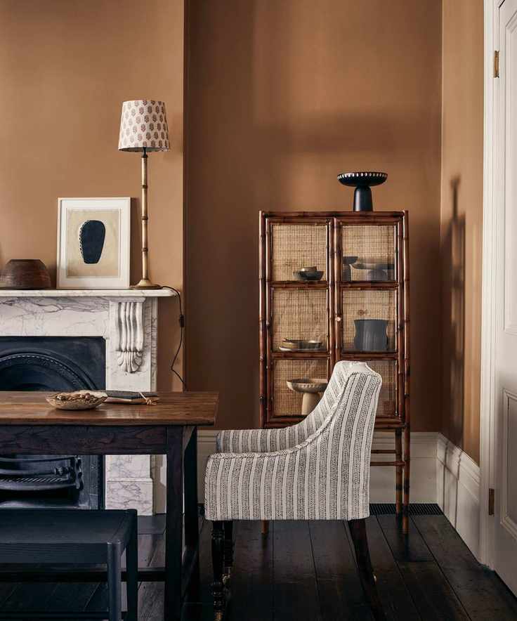 Dining room painted in a dark ochre shade with natural textures and a rustic cabinet