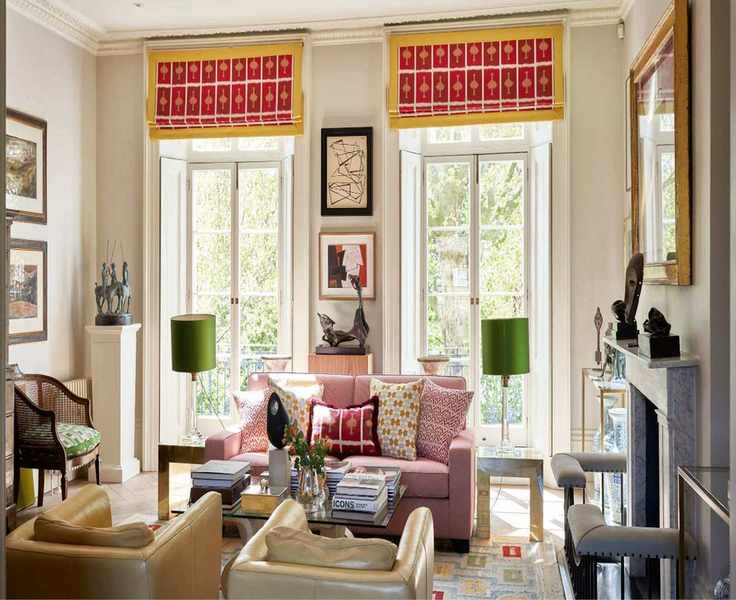 Eclectic living room with large French doors leading to a balcony, featuring pink and yellow blinds, a pink sofa, a coffee table with books and a vase, and two leather armchairs