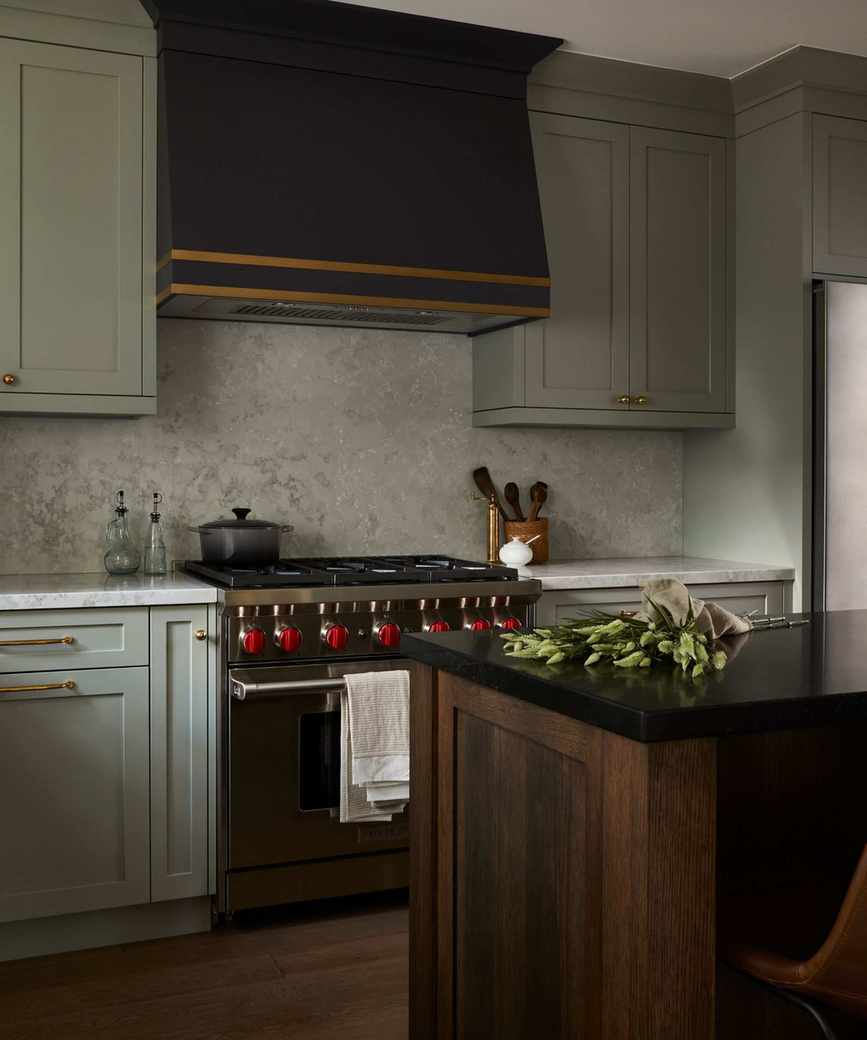 a warm sage green kitchen with a dark custom cooker hood, stainless steel stove, and a wooden kitchen island