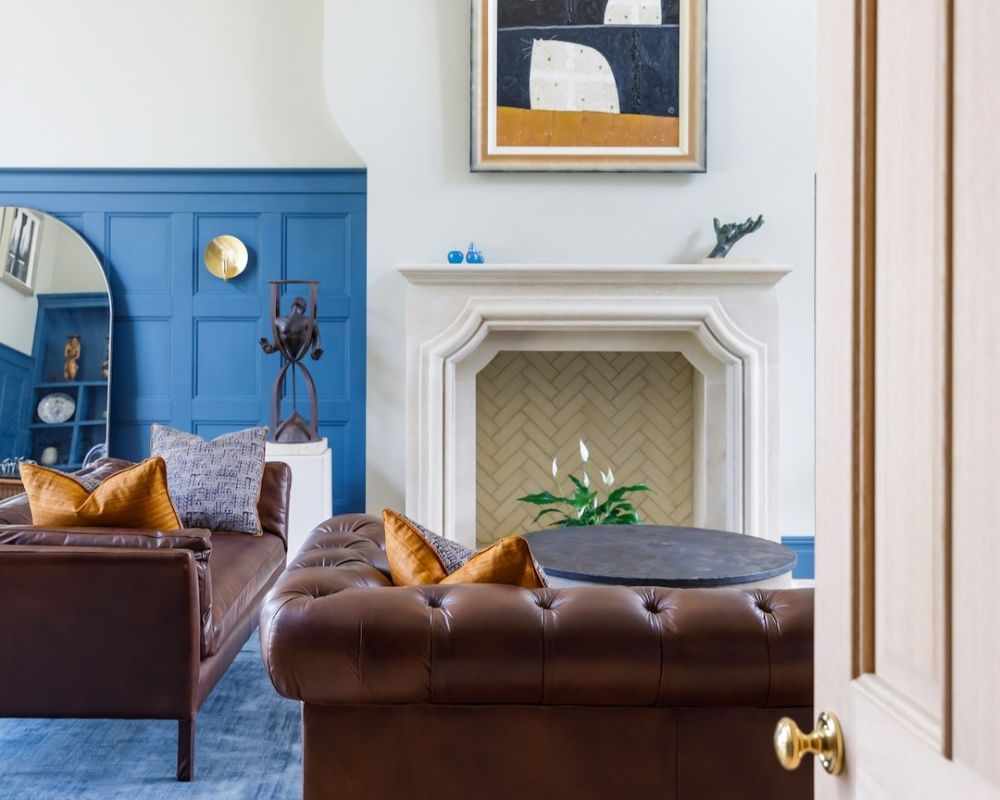 A living room with white walls, blue panels, dark brown couches with throw pillows on, and a blue carpet