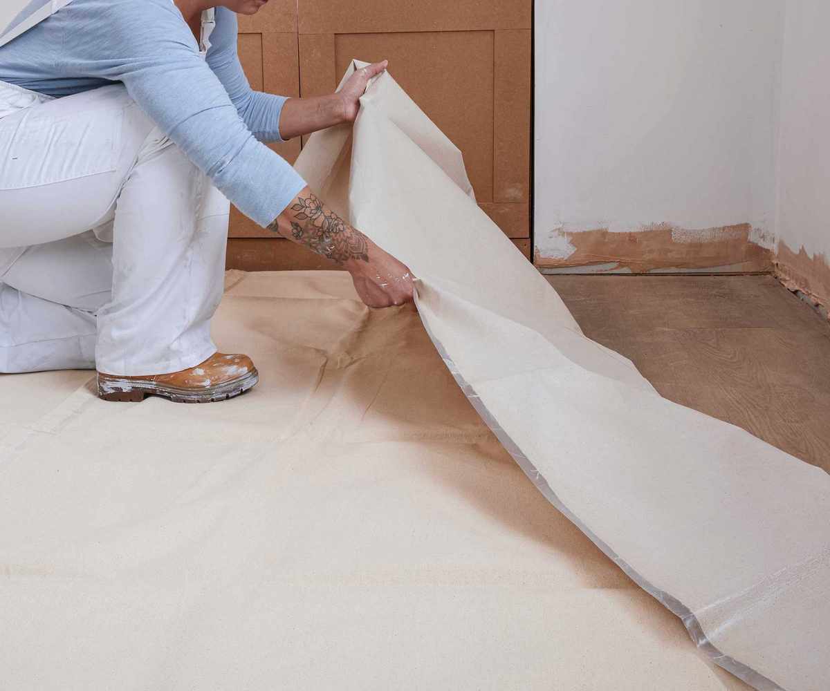 woman in white overalls laying down a dustsheet to decorate