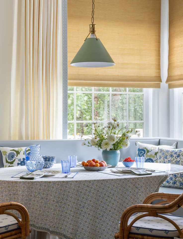 Window area featuring woven bamboo shades layered beneath cream full-length curtains.