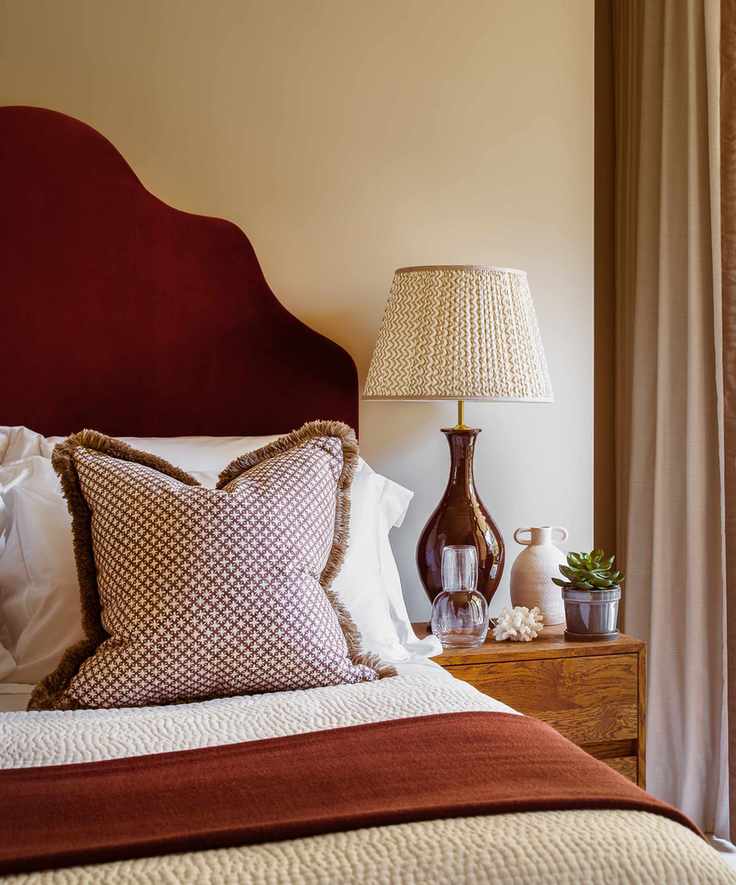 Deep red bedhead and blanket, modern wooden bedside table, brown lamp with patterned lampshade