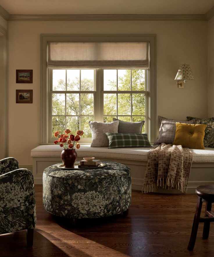 banquette window seat styled for fall with a green tapestry print armchair and ottoman, styled with a tray with books and a vase of orange dried flowers and a mix of fall pillows and blankets