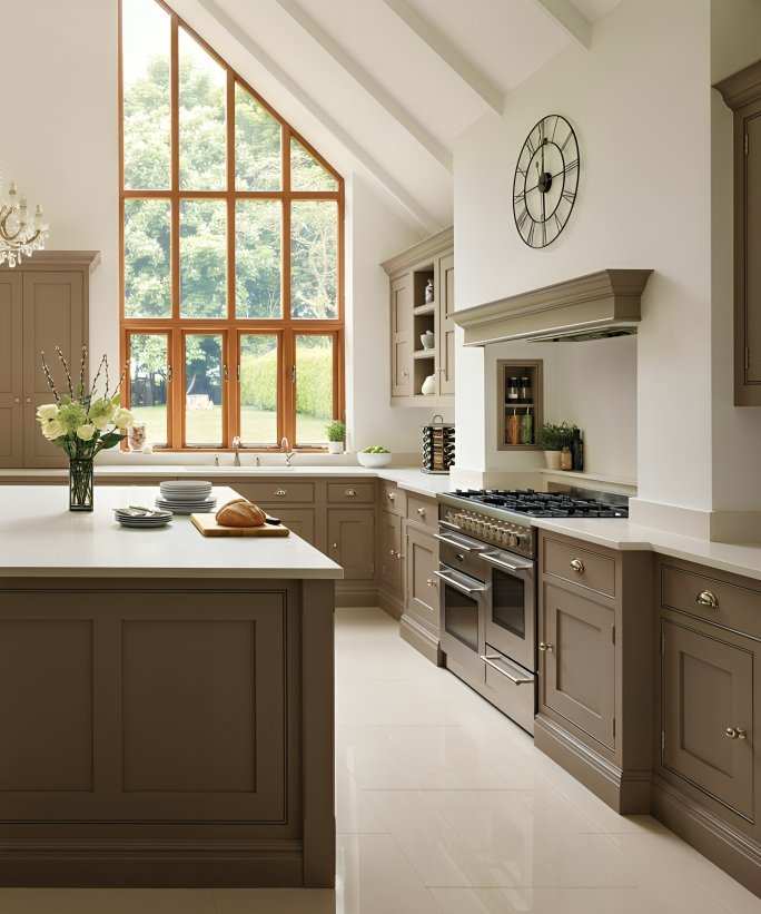 A large open-plan kitchen diner with large floor to ceiling windows, up to a pitched ceiling. Brown kitchen cabinets with an island.