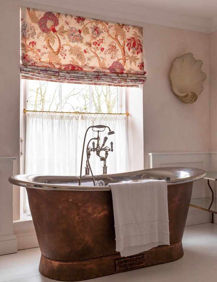 Bathroom window area showcasing a patterned roman shade layered above semi-sheer white cafe curtains.