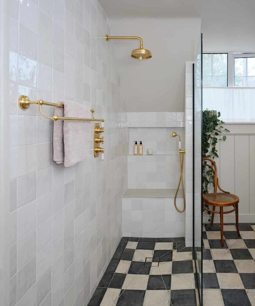 A large white tiled shower with gold hard wear. Black and white checked flooring.
