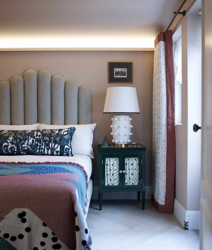 Bedroom with double bed with upholstered headboard, bedside table and lamp, neutral walls and floor