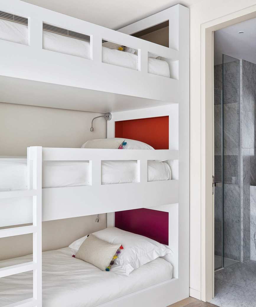 A triple bunk bed painted white with red accents