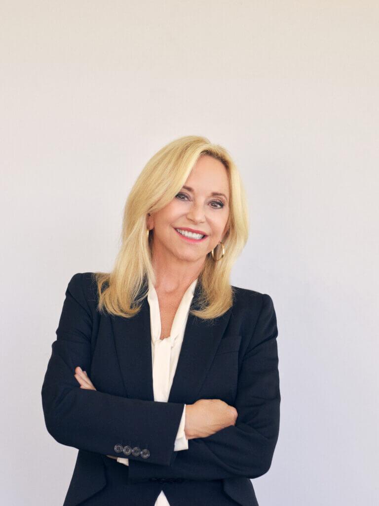 Julie Wainwright, founder of TheRealReal and Ahara smiles and poses in a black blazer. We explore her journey as a female founder 