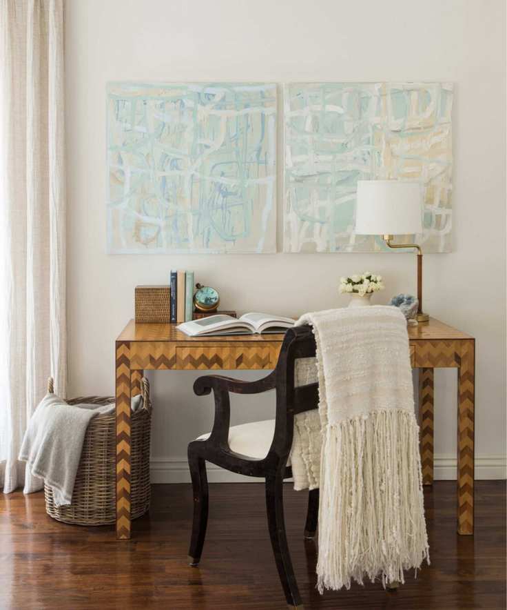 A home office with desk and chair facing wall with lamp and draped blanket