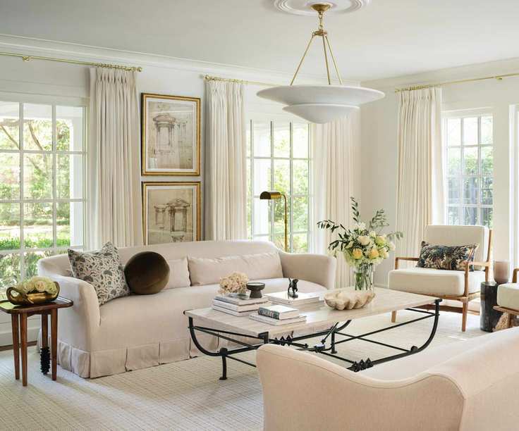 warm minimalist living room with all neutral decor, a wrought iron coffee table, arm chairs with foliage printed cushions and a skirted couch