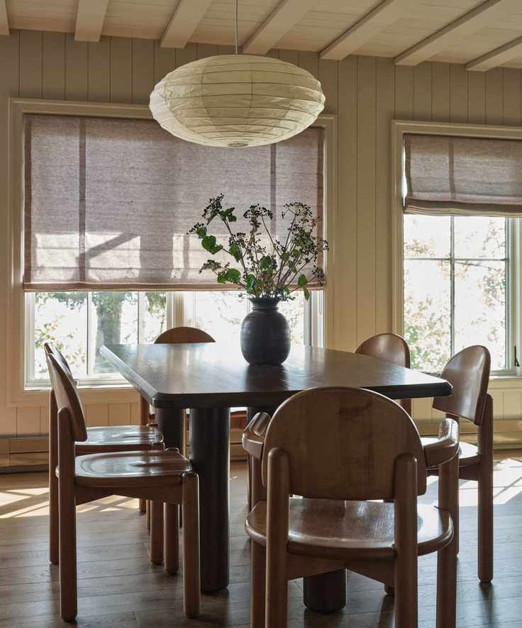 a warm white paneled cottage dining room with wooden table and chairs and a paper lantern