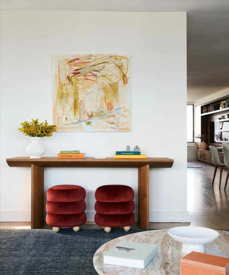 a console table with two red velvet stools underneath, decor on top, and an abstract yellow painting on the wall