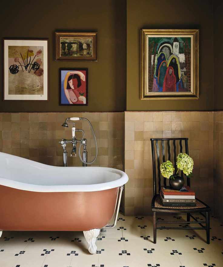 an earthy green bathrom with zellige half height tiles, tiled floor, a rust painted freestanding tub and statement art