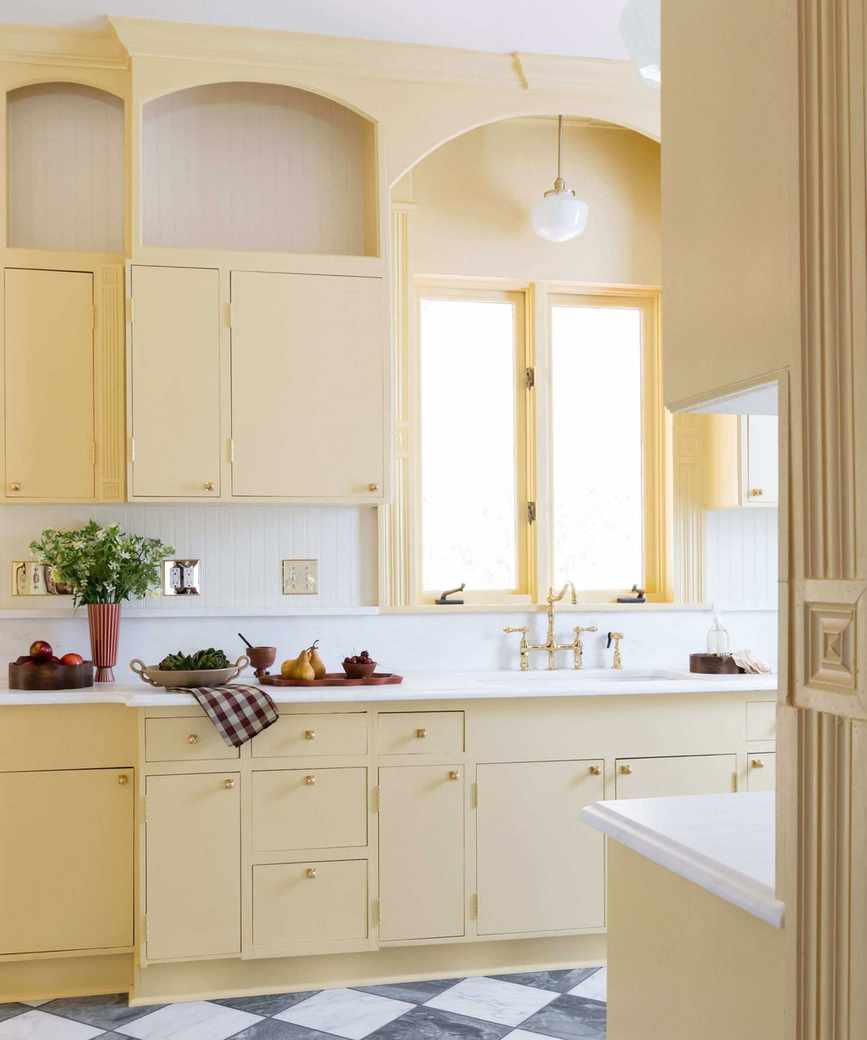 A kitchen drenched in butter yellow paired with white wall tiles and countertops and a black and white checkerboard floor