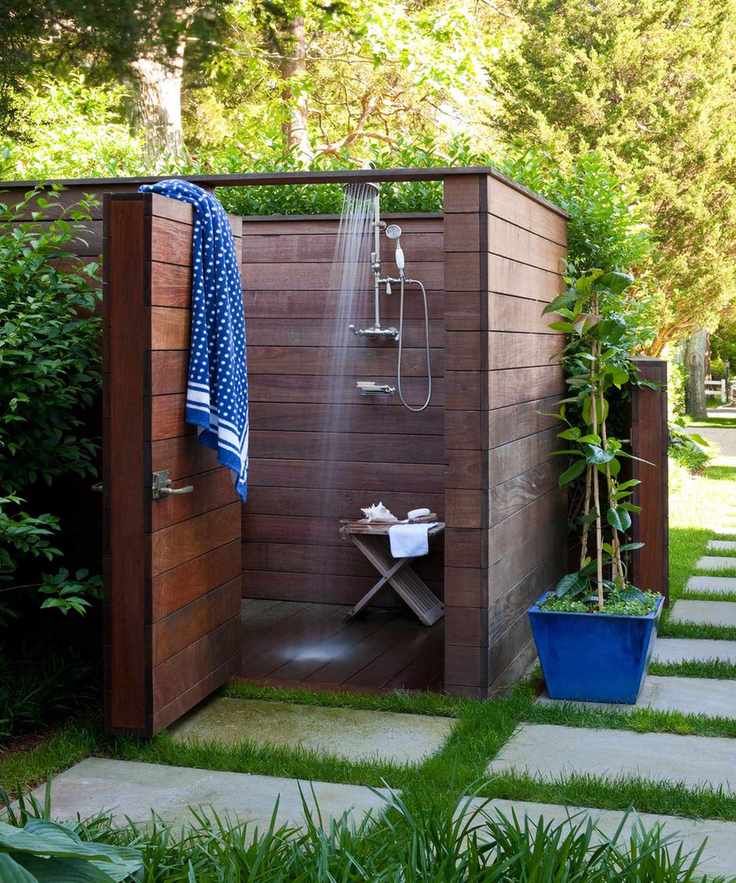 Wooden outdoor shower enclosure in garden with grass between pavers