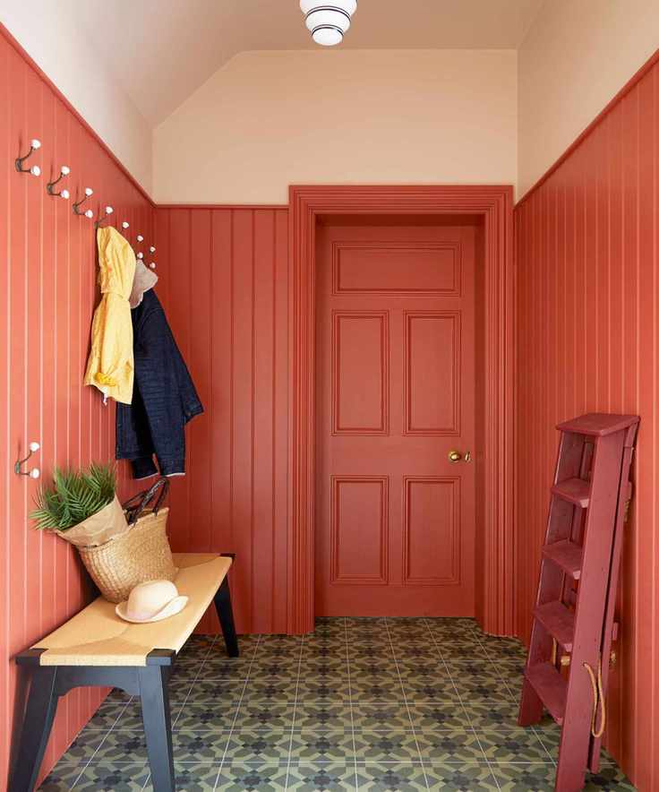 A boot room with panelled walls painted in a vivid coral paint