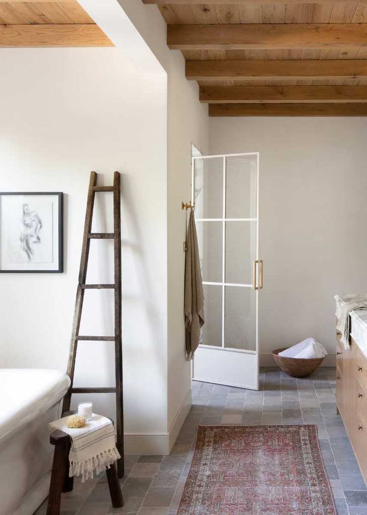 A white-walled bathroom with wooden-beamed ceiling, grey tiled floor, and ladder feature