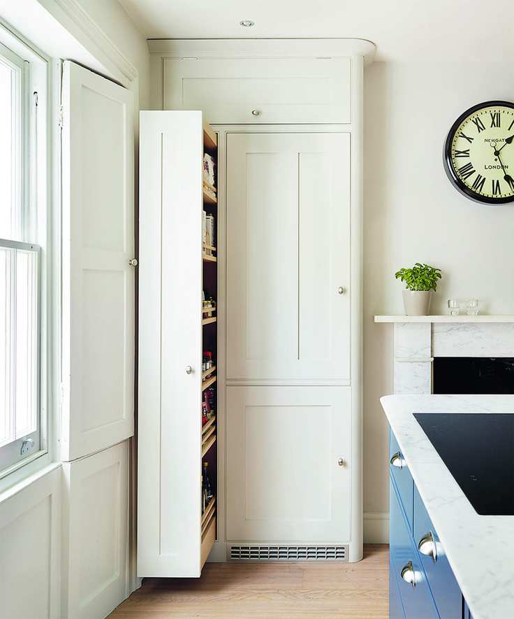 A narrow pull out larder in a traditional white kitchen with a large clock on the wall