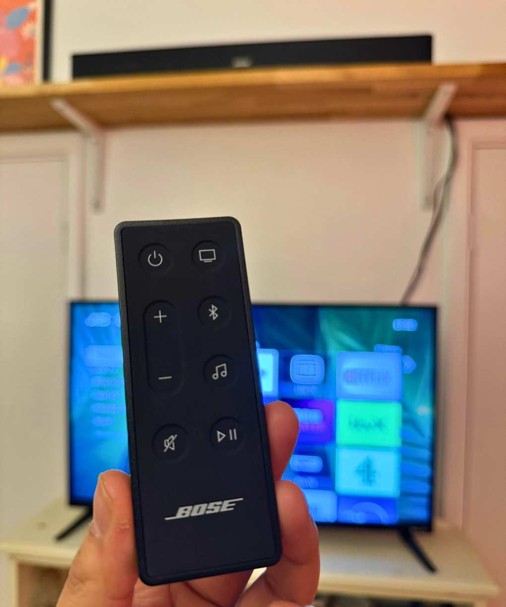 Remote for the Bose Smart Soundbar in front of TV and shelf.