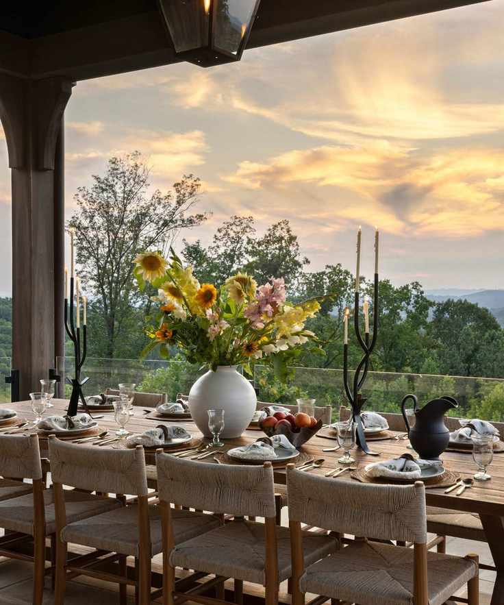 Outdoor dining table under a pergola with flowers on the table and sunset views beyond