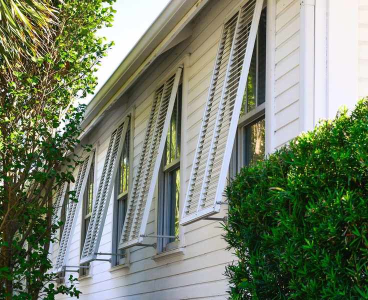 storm shutters on windows on a white sided house, propped open on a sunny day.