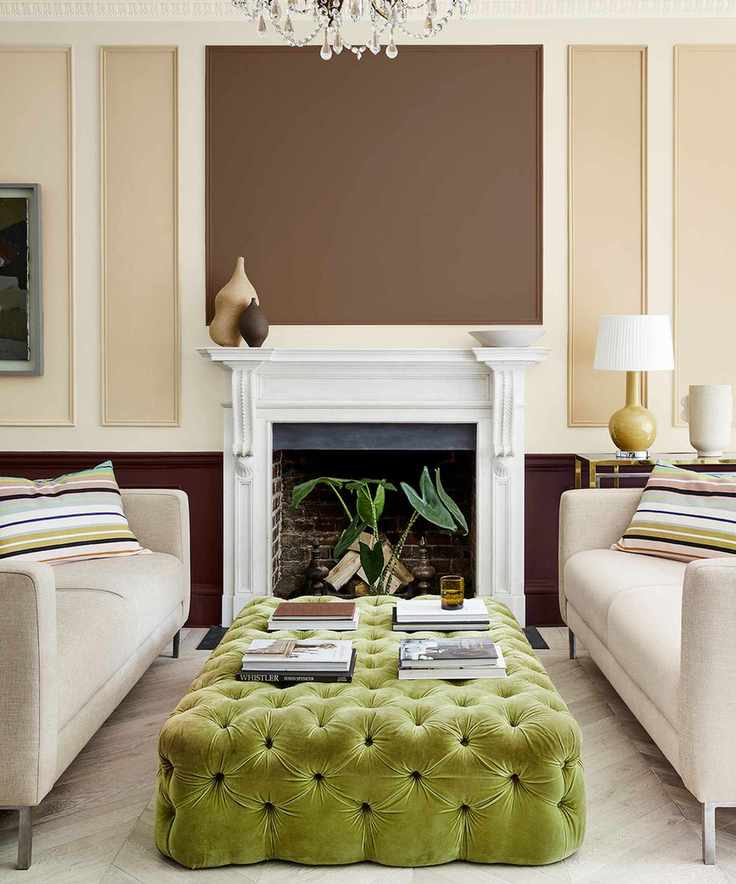 Living room painted in a calming brown and cream palette with white paneling and a bright green tufted ottoman between two cream sofas.