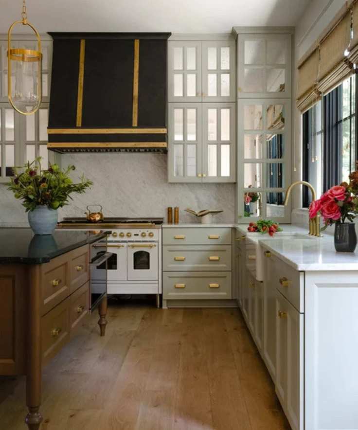 A traditional kitchen with pastel green cabinets, a wooden island, and mirrored panels in the upper cabinets