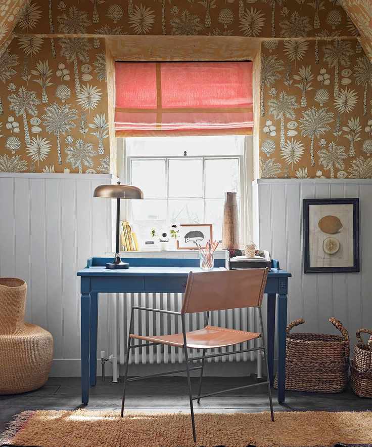 Workspace featuring a blue desk, leather chair, ochre floral wallpaper, light blue paneling, and woven baskets
