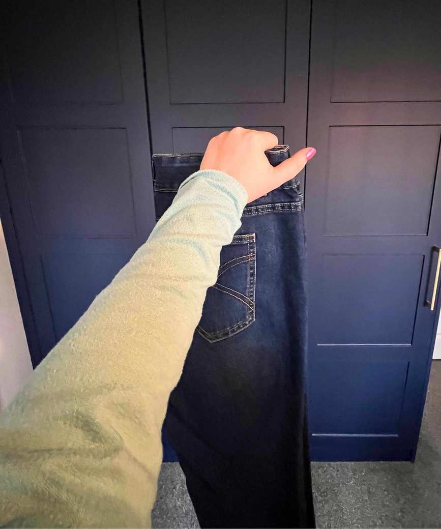 Pictured is the pair of jeans now folded vertically so the zip falls inside and a hand holding the top of the waist
