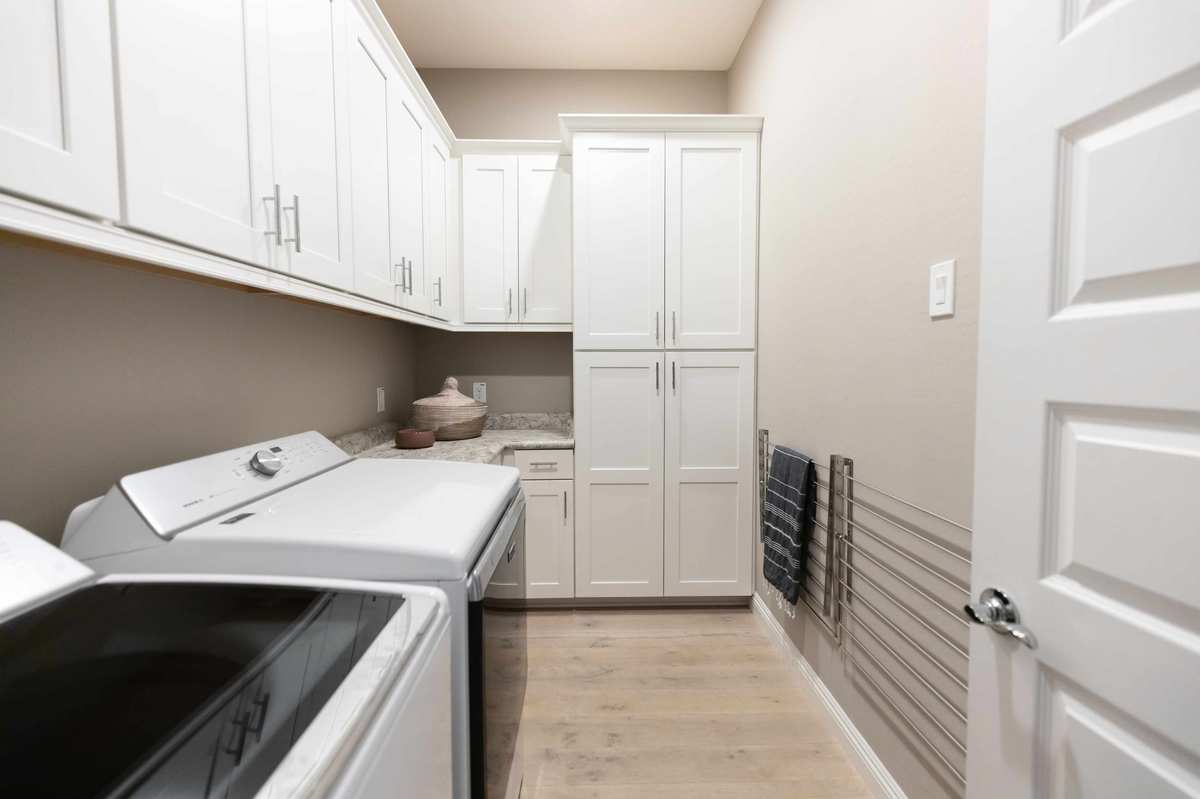 Narrow utility room with white cabinets and horizontally laid wooden flooring