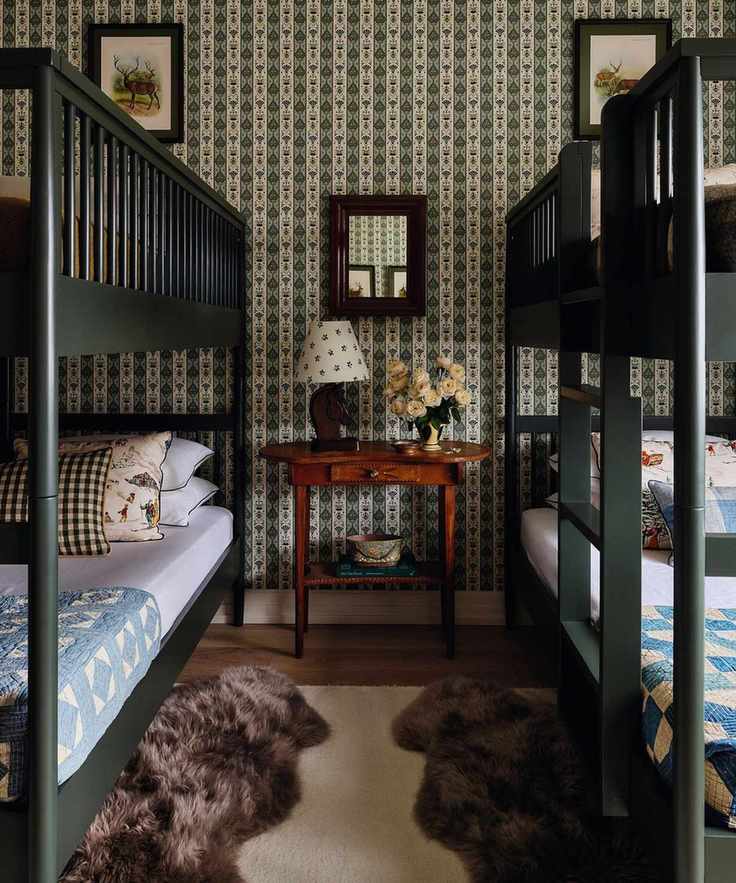 a green floral wallpapered bedroom with two dark green bunk beds, layered rugs, plaid pillows and patchwork blankets style the beds