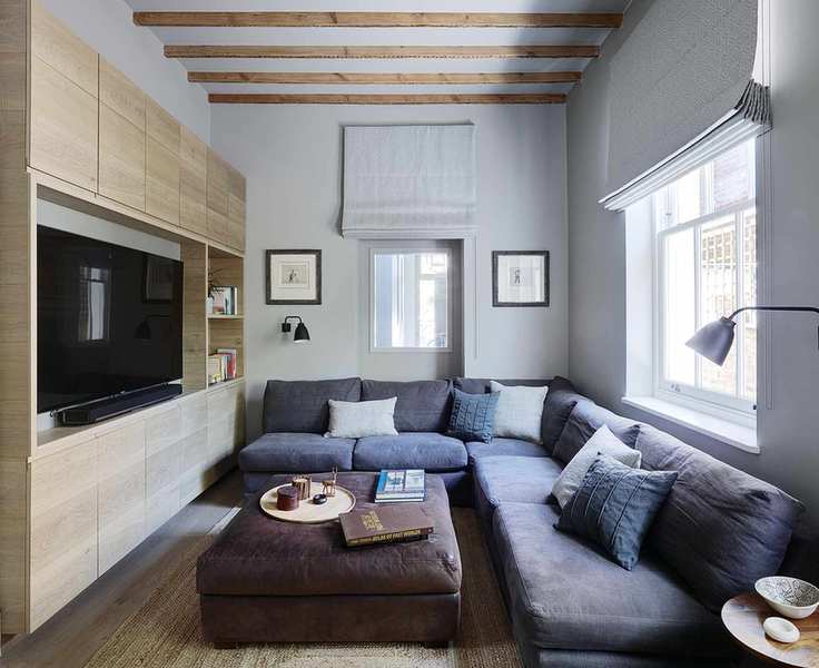 Living room featuring a large gray L-shaped sofa, ottoman, and built-in cupboards with a television