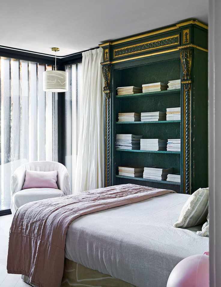 A small bedroom with pink bed linens and a green painted bookcase.