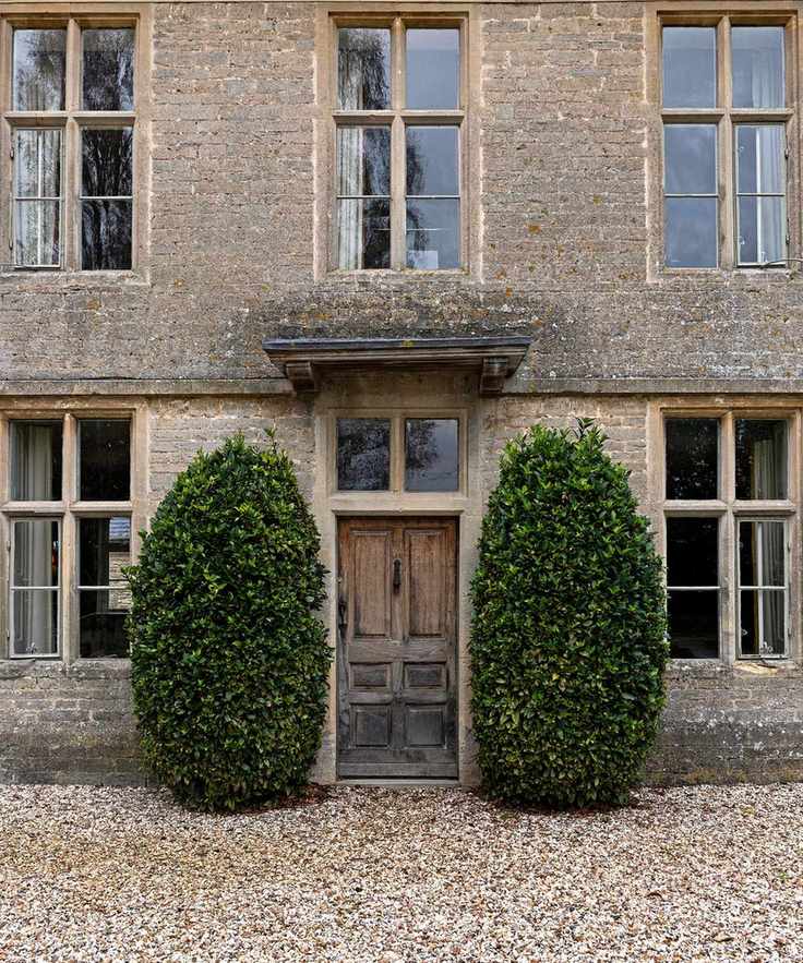 A period home with a wooden front door with two bushes on either side and a gravel path