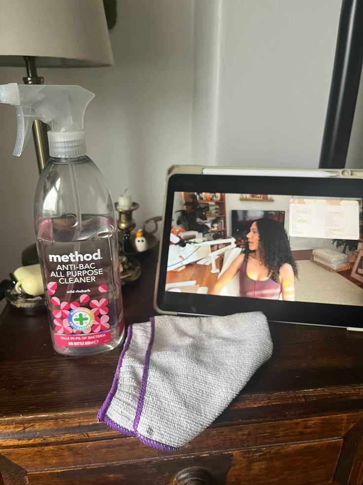 A bottle of pink method cleaning spray on a night stand beside an Ipad and a microfiber cleaning cloth