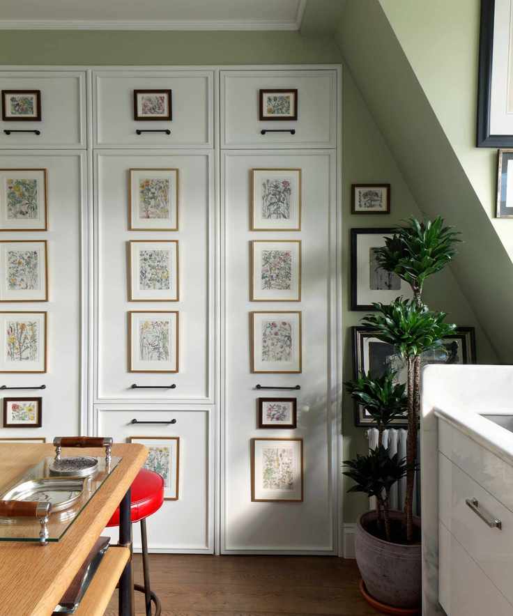 green painted kitchen with wooden table and panelled storage doors with artworks on