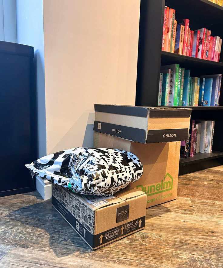 Stack of boxed items on the floor next to a color-coordinated bookshelf