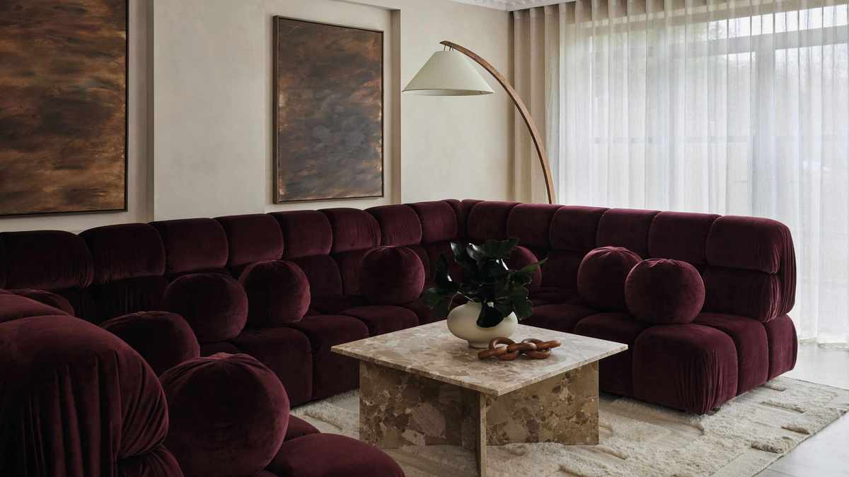 A stunning living area designed by Amy Stoddart, featuring a deep plum velvet tufted sectional sofa and a square marble coffee table on a textured cream rug.