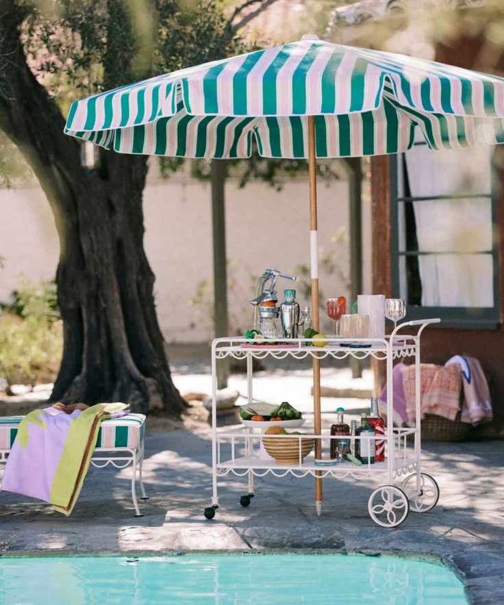 poolside retro style scalloped wrought iron bar cart serving up cocktails with a green and pink striped patio umbrella